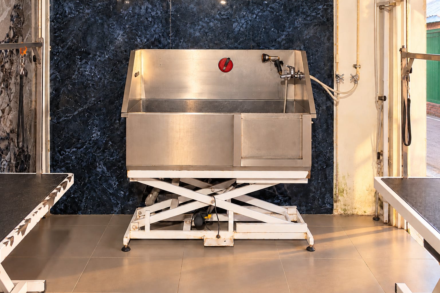 The grooming room: a stainless steel bathing tub on a lift between two grooming tables, with dark marble walls