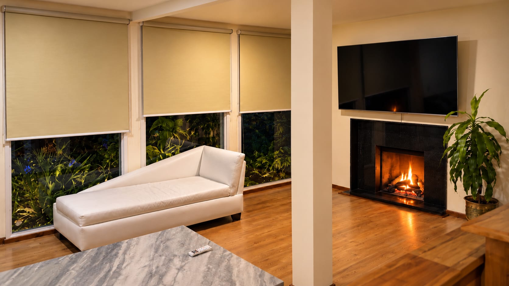 The homestay lounge: a white chaise by tall windows, a central white column, and a fire lit below the television